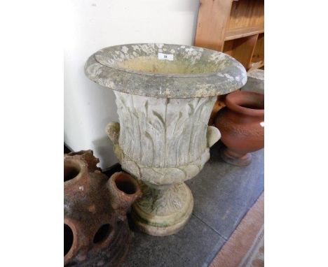 A large stone garden urn with leaf decoration, fitted twin handles, on circular leaf decorated base