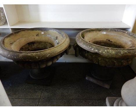 A pair of concrete garden urns with ring form handles, on turned pedestals and square bases