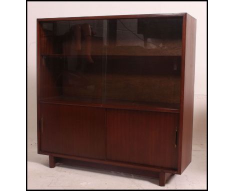 A vintage mid century bookcase unit with upper glass sliding doors, lower sliding doors with brass detailed handles and raise