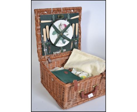 A collection of vintage linens and cloths all being contained within a vintage whicker picnic hamper