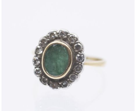 An emerald and diamond 18c gold cluster ring, comprising a central rub over set oval emerald within a border of round brillia