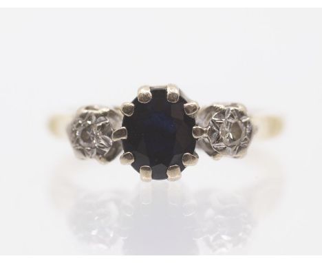 A sapphire and diamond three stone 18ct gold ring, the central oval cut sapphire set between two small illusion set diamonds,