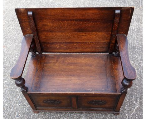 A 1930?s oak monks bench of typical form with plain top and seat over a carved panel front, 95cm wide 