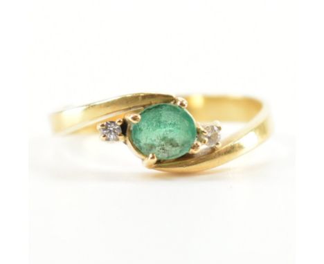 A vintage gold, emerald and white stone crossover ring. The ring being set with an oval cut emerald flanked by two round cut 