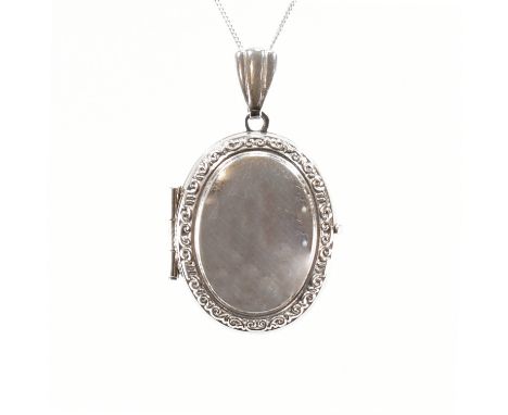 A 9ct white gold locket pendant &amp; necklace chain. The locket of oval form with scrolling pattern to the border &amp; hing