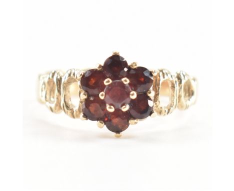 A hallmarked 9ct yellow gold &amp; red stone cluster ring. The ring having a central round cut dark red stone surrounded by a