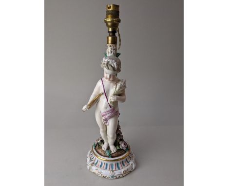 A 19th century porcelain candlestick converted to a table lamp, depicting a cherub representing Harvest, holding a scythe and