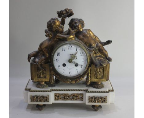 A gilt metal and marble mantle clock, the case flanked with winged cherubs, the base raised on metal feet, 4 inch enamel dial