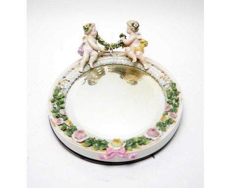 A Sitzendorf ceramic table mirror, the oval bevelled mirror plate within frame moulded with flowering foliage and a pair of p