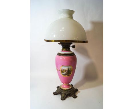 A 19th century porcelain oil lamp painted with landscapes within gilded line borders on a pink ground with flared base and ma
