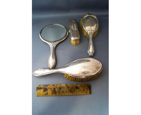 A silver backed hand mirror; three silver backed brushes; and a plastic comb