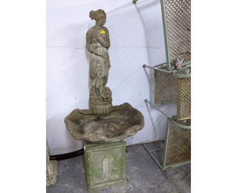 A weathered concrete stone garden fountain in the form of a classically dressed maiden with a vase by her feet, mounted on a 