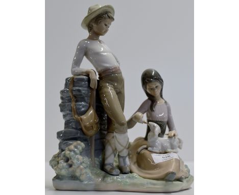 AN 11" LLADRO PORCELAIN DOUBLE FIGURINE CENTREPIECE MODELLED AS A YOUNG GIRL & BOY FEEDING A NEW BORN LAMB     