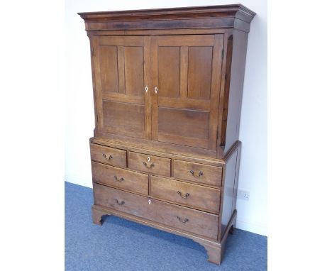 An 18th century oak press cupboard, the outset cornice above a mahogany frieze and two panelled doors enclosing shelves, furt