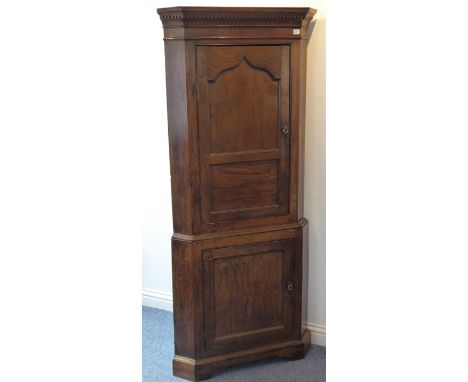 A late-18th century, George III period, freestanding oak corner cupboard; the dentil cornice above panelled door and one furt