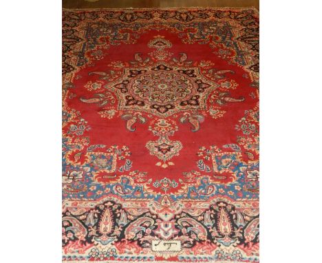 A red ground Keshan carpet, decorated with teardrop medallion to centre within floral borders, fringed, signed 'Farang' in Fa