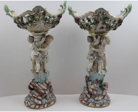 A pair of Meissen porcelain baskets on stands, pierced and floral encrusted oval baskets, raised upon putti stems, supporting