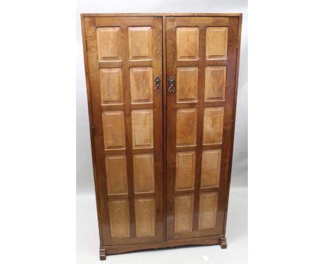 A first quarter 20th Century English Arts and Crafts chestnut two door wardrobe, a pair of multi panel doors opening to revea