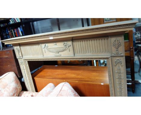 A GEORGE III STYLE PINE FIRE SURROUND of neoclassical design, carved with bell flowers, ribbons anthemion and an urn, the she