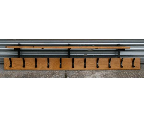 A set of eleven coat hooks mounted on an oak plaque with shelf above.