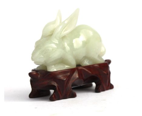 A jade / hardstone figure of recumbent hare on a wooden stand, 7cms (2.75ins) long.