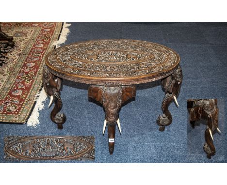 Indian Carved Oval Teak High Table, the top profusely carved with elephants and Indian deities supported on an elephant trunk