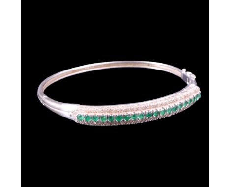 An emerald and diamond hinged bangle, comprising a row of round-cut emeralds claw-set above and between rows of diamond brill