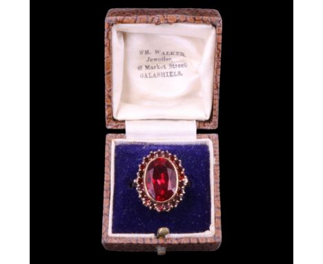 A Verneuil ruby ring, the oval stone of approx 14 mm x 6 mm bezel-set and framed by small round-cut red paste stones on a 9 c