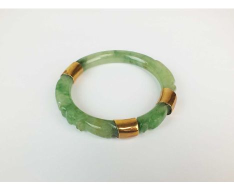 A carved jade bangle, with three yellow metal mounts, not stamped, 7.5cm diameterProvenance: Property of a Titled Estate
