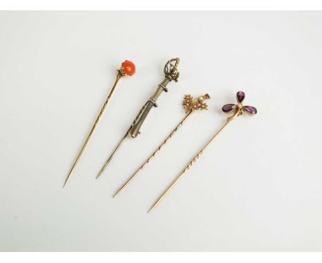 An amethyst and split seed pearl stick pin, designed as a clover, together with a single coral set stick pin, a seed pearl se