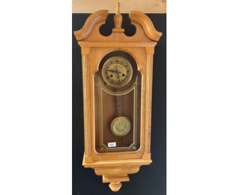 Light oak cased wall clock, Ornate brass style face and matching pendulum. Comes with key. [Will not post] [98CM in length] [
