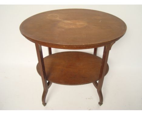 An Edwardian mahogany Sheraton Revival oval two tiered occasional table.
The top inlaid with patterae, on shaped outswept sup