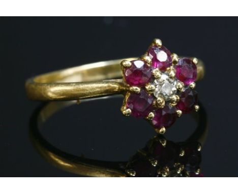 An 18ct gold, diamond and ruby cluster ring, with an old Swiss cut diamond, claw set to the centre. A border of circular mixe