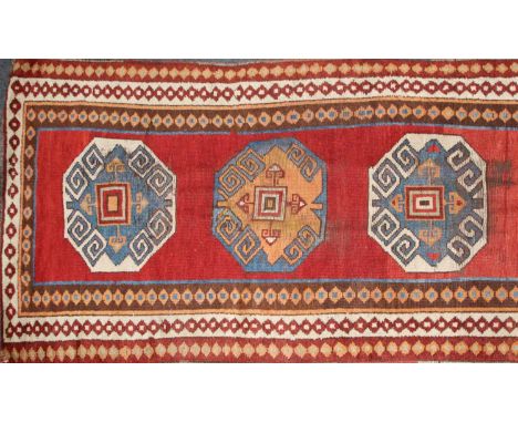An eastern runner rug, probably Caucasian, the centre panel with geometric cartouches on a red ground, within a triple geomet