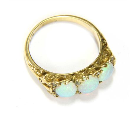 A three stone opal ring, the cabochon stones in scrolling claw mounts, with diamond chips to the corners, the shank marked 18