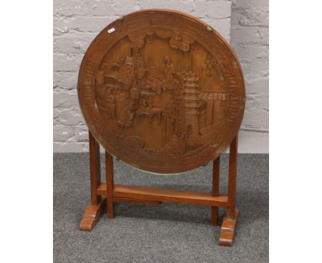 An oriental carved tilt top occasional table with glass top raised on gate leg supports.