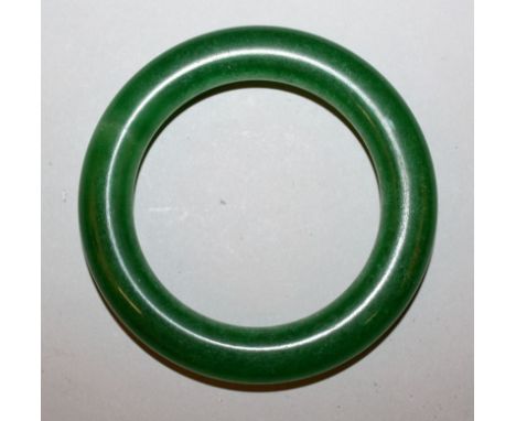 A CHINESE GREEN JADE-LIKE BANGLE, 3.3in diameter, the inner rim 2.25in diameter.