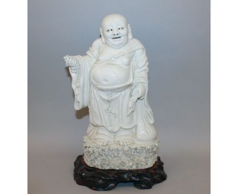 A 19TH CENTURY CHINESE BLANC-DE-CHINE PORCELAIN FIGURE OF BUDAI, together with a fitted wood stand, the deity standing on a r