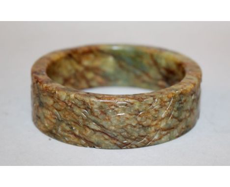 AN UNUSUAL CHINESE JADE BANGLE, 19th Century or earlier, the stone of underlying green tone with dense brown and russet stria