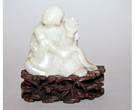 A CHINESE JADE MODEL OF A SEATED MONK, together with a fitted wood stand, the monk bearing aloft a libation bowl, 3.5in high 