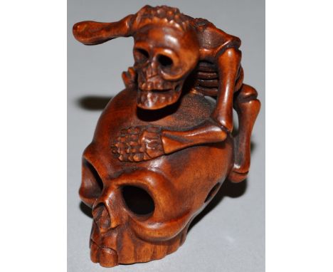 A BOXWOOD NETSUKE, A SKELETON ON A SKULL, signed.