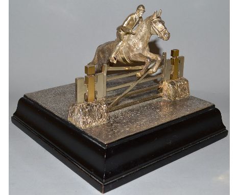 A CAST SILVER SHOW JUMPING MODEL, horse and rider jumping a field gate. 7.5ins x 7ins, 5ins on a wooden base.London 1963. Mak