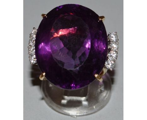 A LARGE AMETHYST OVAL RING with four diamonds to each shoulder, set in yellow gold.