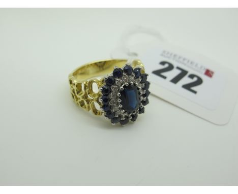 A Large Sapphire and Diamond Cluster Dress Ring, oval claw set to the centre, within two row border of circular sapphires and