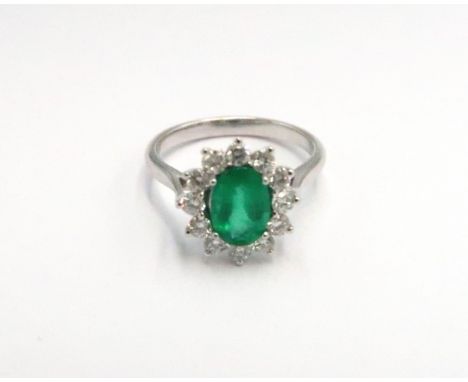 A platinum emerald and diamond dress ring - The central oval cut emerald surrounded by 12 diamonds - ring size M - weight app