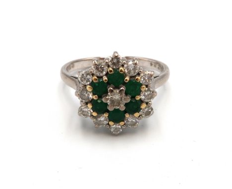 A vintage 18ct white gold, emerald and diamond flowerhead ring, set with central diamond surrounded by six emeralds and twelv