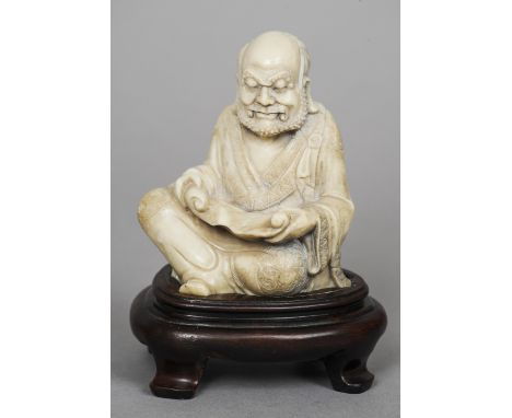 A 19th century Chinese carved soapstone figure of Lohan 
Modelled seated with a scroll, standing on a carved hardwood plinth 