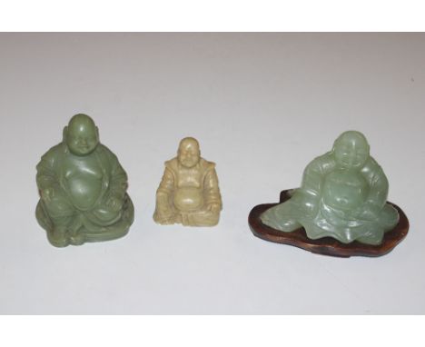 A jade type Buddha on wooden stand together with two others 