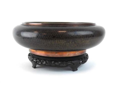 A cloisonne shallow bowl of circular form allover decorated with swirls and flowerheads on a famille noir ground on a carved 