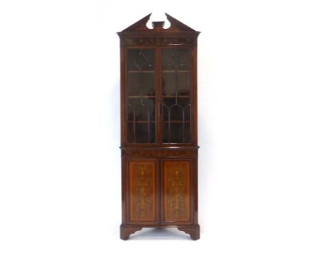 An Edwardian mahogany, strung and marquetry corner cabinet, the architectural pediment over two glazed doors and two solid do